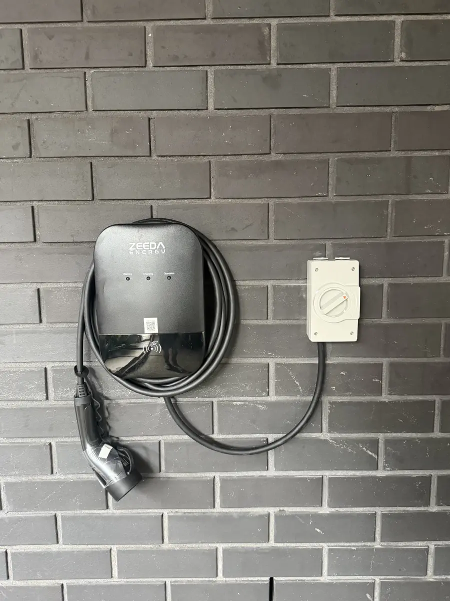 Wall mounted EV charger and isolator installed on a brick home by Pender Electrical